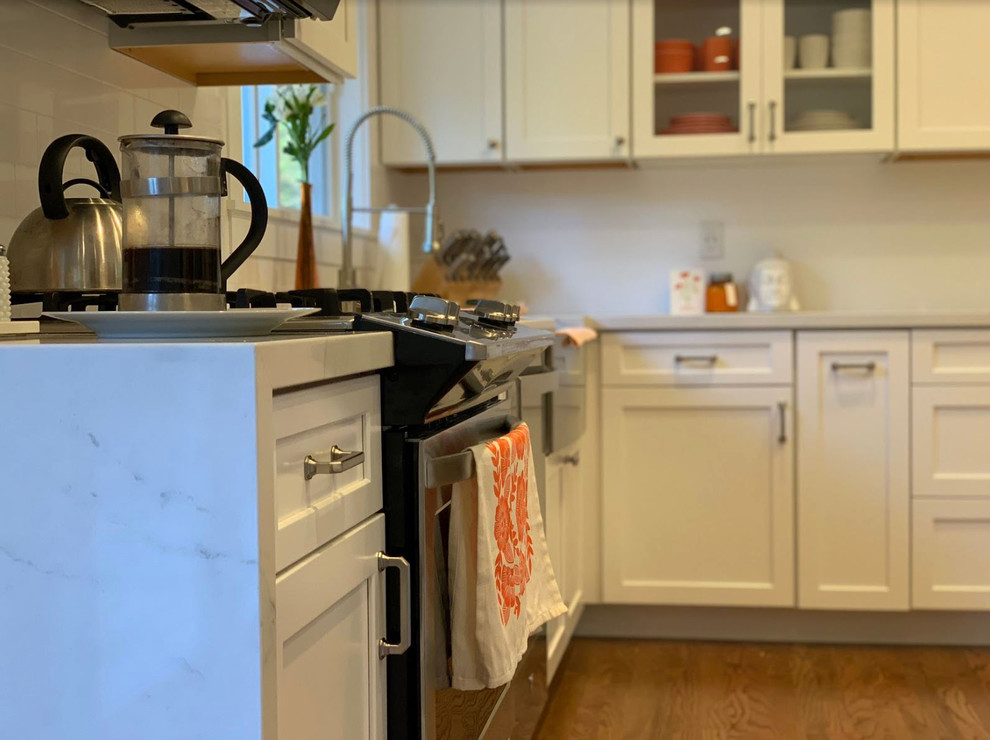 Example of a mid-sized mountain style brown floor eat-in kitchen design with a farmhouse sink, raised-panel cabinets, white cabinets, quartz countertops, white backsplash, stainless steel appliances, an island and white countertops