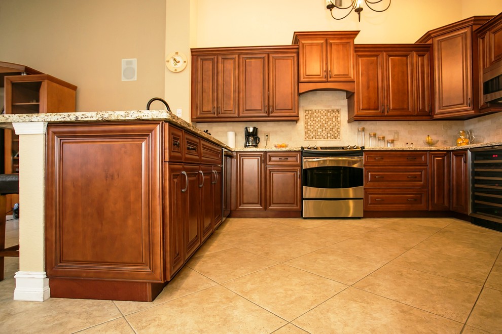 Mid-sized transitional u-shaped porcelain tile eat-in kitchen photo in Miami with an undermount sink, raised-panel cabinets, brown cabinets, granite countertops, beige backsplash, stone tile backsplash, stainless steel appliances, beige walls and a peninsula