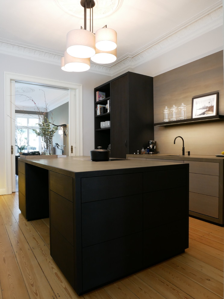 Photo of a mid-sized contemporary galley separate kitchen in Hamburg with a drop-in sink, flat-panel cabinets, black cabinets, brown splashback, black appliances, medium hardwood floors, with island, brown floor and black benchtop.