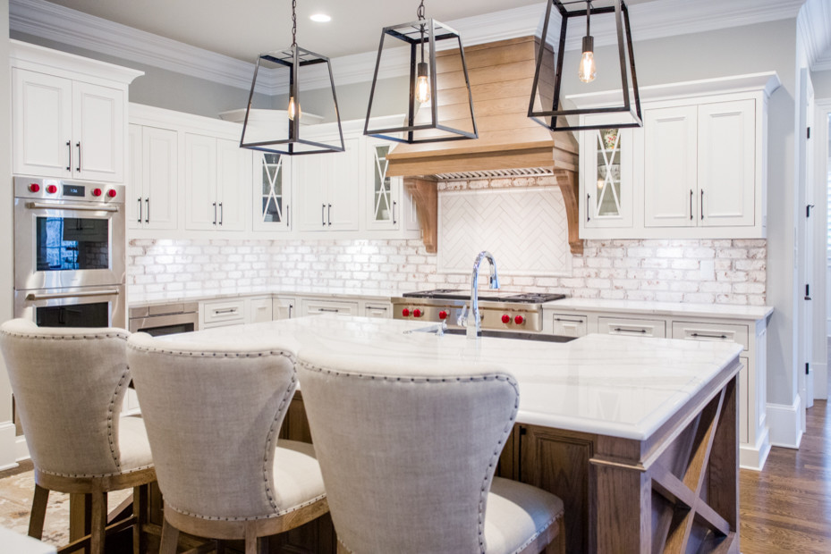 Example of a large transitional u-shaped medium tone wood floor and brown floor eat-in kitchen design in Atlanta with a farmhouse sink, raised-panel cabinets, white cabinets, quartz countertops, white backsplash, brick backsplash, stainless steel appliances, an island and white countertops