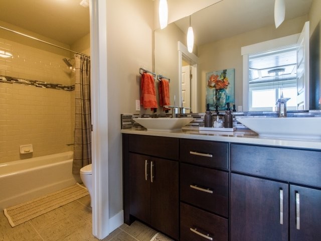 Photo of a mid-sized transitional kids bathroom in Salt Lake City with gray tile, beige walls, a vessel sink, flat-panel cabinets, dark wood cabinets, quartzite benchtops, an alcove tub, a shower/bathtub combo, a one-piece toilet, mosaic tile and porcelain floors.