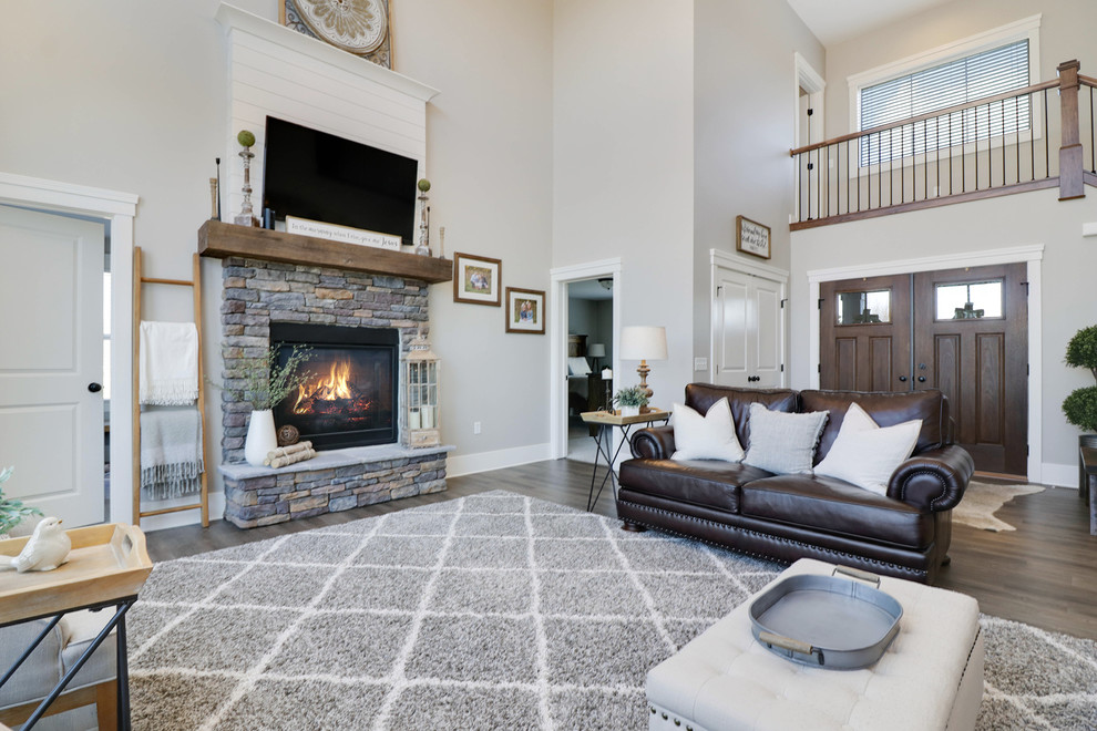 This is an example of a large country formal open concept living room in Grand Rapids with grey walls, medium hardwood floors, a standard fireplace, a stone fireplace surround, a wall-mounted tv and brown floor.