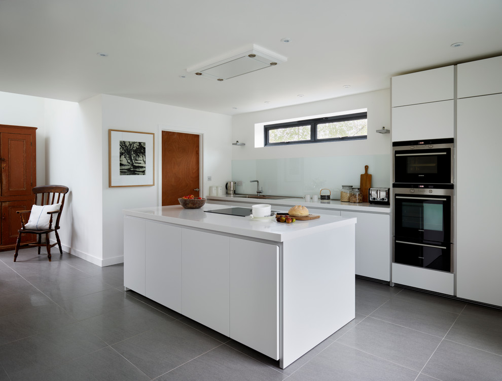 This is an example of a modern open plan kitchen in Wiltshire with a single-bowl sink, flat-panel cabinets, white cabinets, laminate benchtops, white splashback, glass sheet splashback, black appliances, porcelain floors and with island.