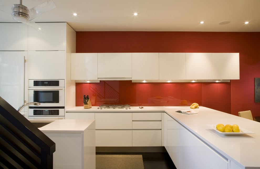 Modern kitchen in DC Metro with white appliances, an undermount sink, flat-panel cabinets, white cabinets, red splashback and glass sheet splashback.