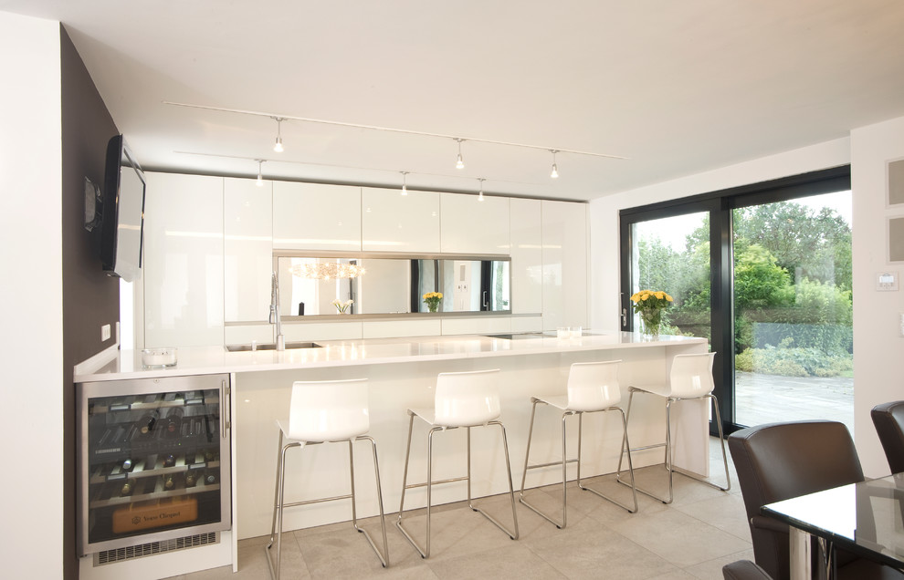 Photo of a mid-sized contemporary galley open plan kitchen in Nuremberg with a drop-in sink, flat-panel cabinets, white cabinets, solid surface benchtops, mirror splashback, porcelain floors and with island.