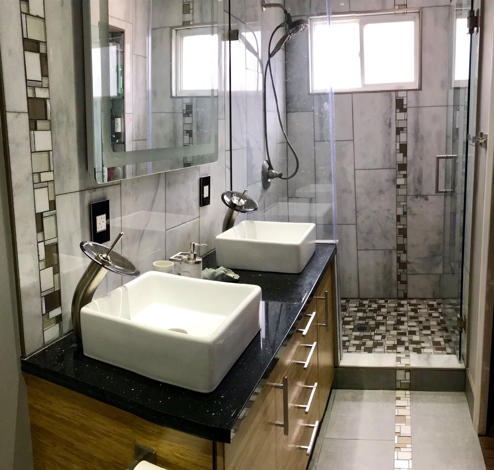 This is an example of a modern master bathroom in San Francisco with flat-panel cabinets, medium wood cabinets, an alcove shower, a one-piece toilet, white tile, marble, a vessel sink, granite benchtops, a hinged shower door and black benchtops.