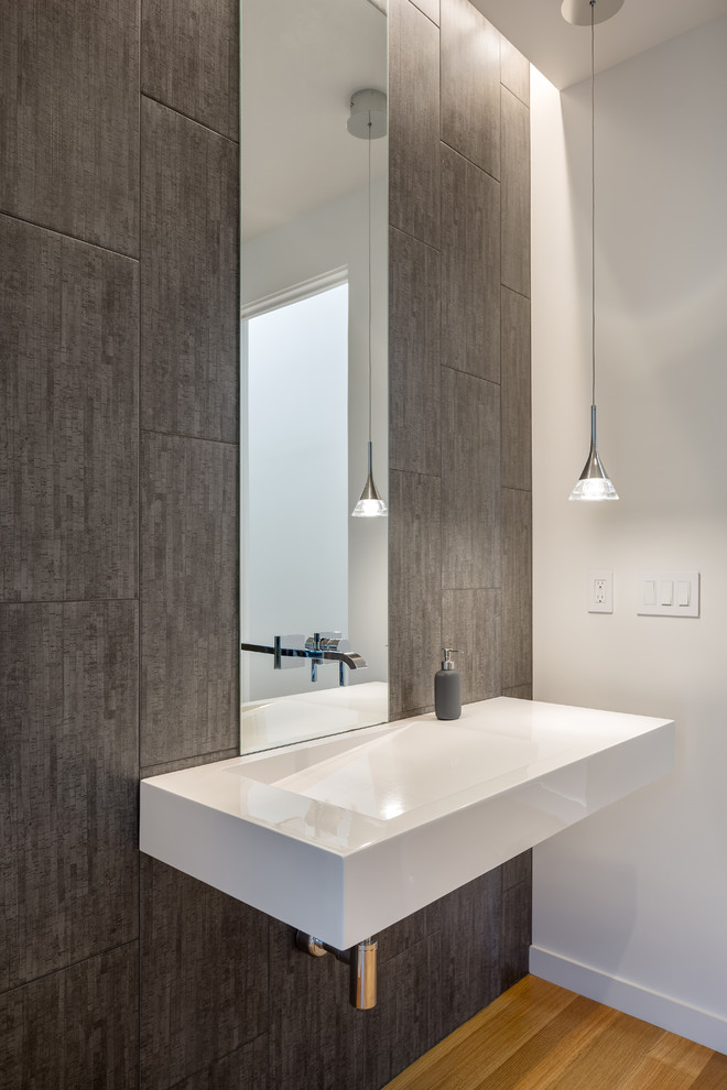 Photo of a modern powder room in Portland with gray tile, white walls, medium hardwood floors, a wall-mount sink and brown floor.