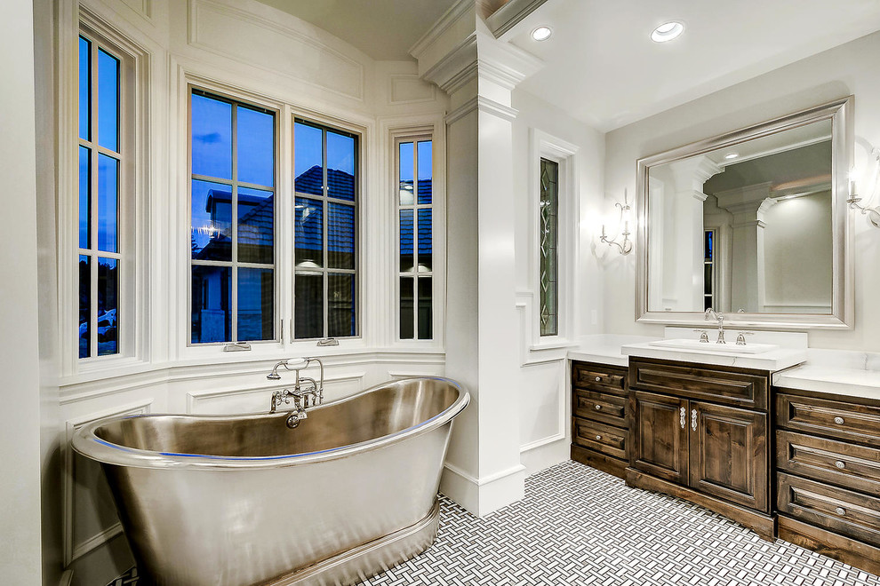 This is an example of an expansive master bathroom in Denver with raised-panel cabinets, dark wood cabinets, a freestanding tub, an alcove shower, white walls, cement tiles, a drop-in sink, marble benchtops, multi-coloured floor, a hinged shower door and white benchtops.