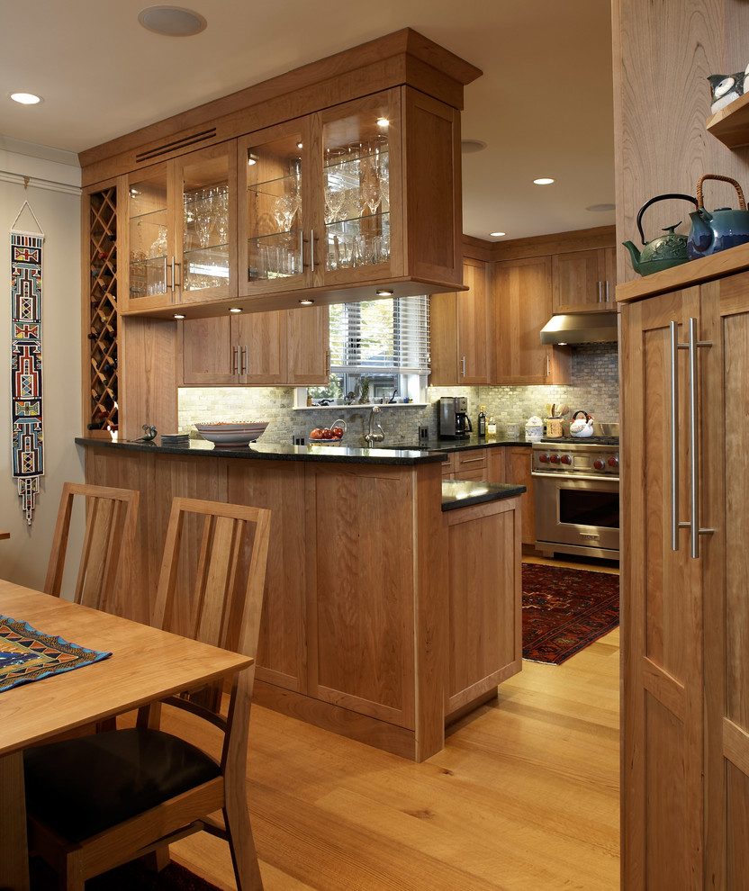 Photo of a mid-sized traditional u-shaped eat-in kitchen in Boston with shaker cabinets, medium wood cabinets, grey splashback, stainless steel appliances, light hardwood floors, a peninsula, beige floor and black benchtop.