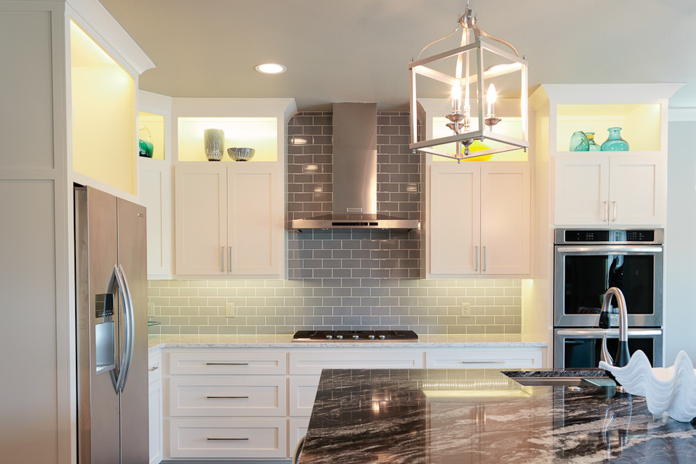 Example of a mid-sized beach style u-shaped dark wood floor eat-in kitchen design with an undermount sink, shaker cabinets, white cabinets, granite countertops, gray backsplash, glass tile backsplash, stainless steel appliances and an island
