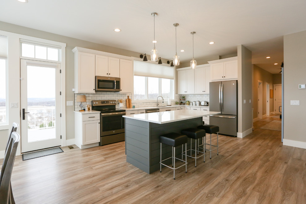 Inspiration for a large transitional u-shaped light wood floor and brown floor eat-in kitchen remodel with an undermount sink, recessed-panel cabinets, white cabinets, quartz countertops, white backsplash, subway tile backsplash, stainless steel appliances, an island and white countertops