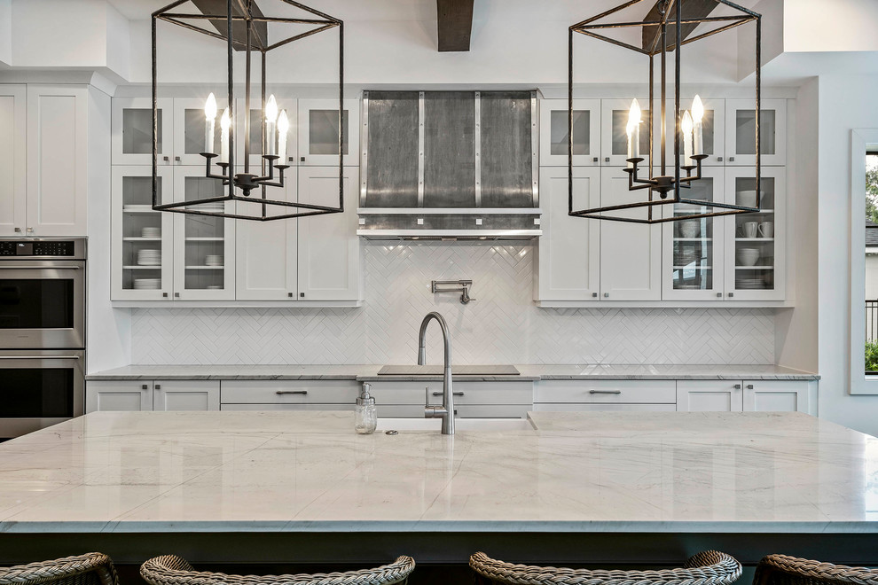 Large transitional l-shaped medium tone wood floor eat-in kitchen photo in Orlando with a farmhouse sink, glass-front cabinets, white cabinets, marble countertops, white backsplash, mosaic tile backsplash, stainless steel appliances, an island and white countertops