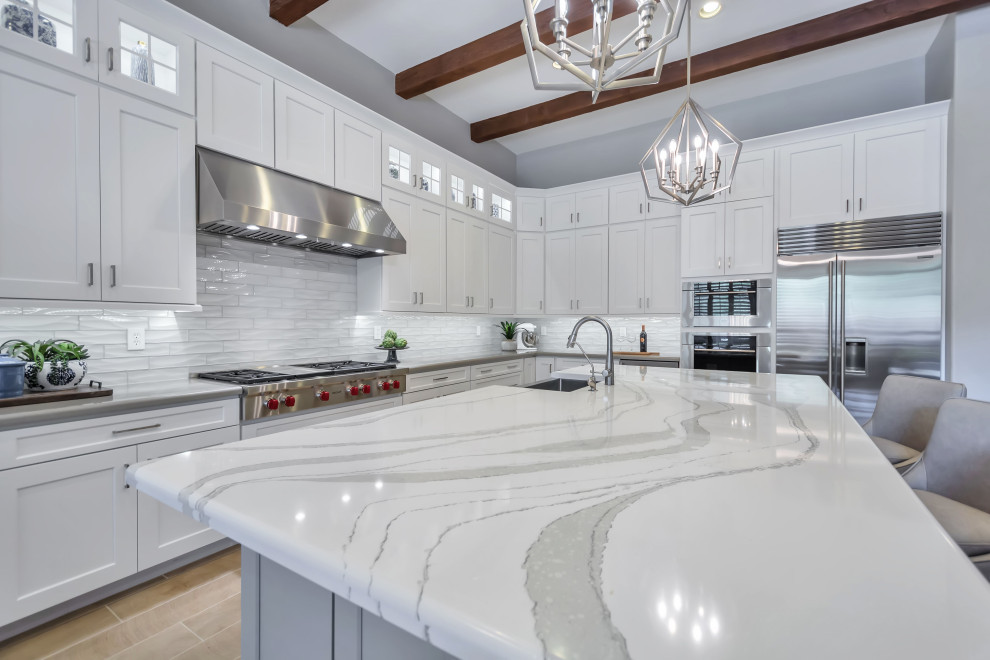 Inspiration for a large transitional u-shaped separate kitchen in Phoenix with a farmhouse sink, shaker cabinets, white cabinets, quartz benchtops, white splashback, glass tile splashback, stainless steel appliances, porcelain floors, with island, beige floor, white benchtop and exposed beam.