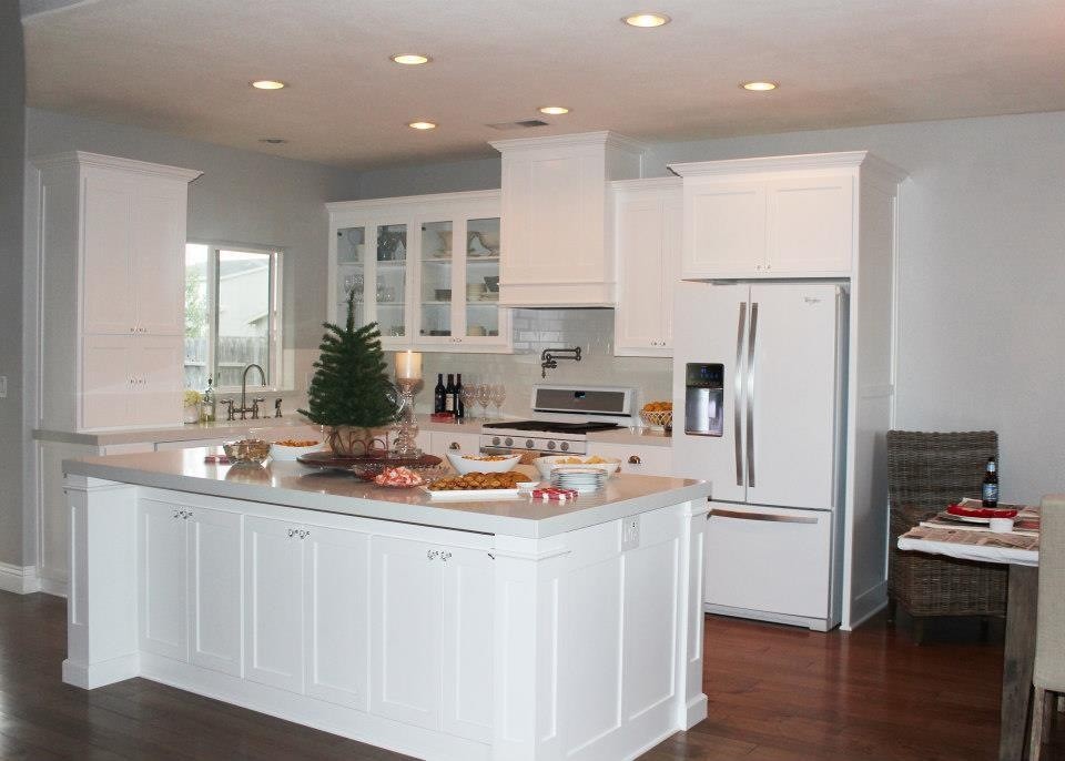 Mid-sized l-shaped dark wood floor eat-in kitchen photo with a farmhouse sink, shaker cabinets, white cabinets, white backsplash, subway tile backsplash, white appliances, gray walls and an island