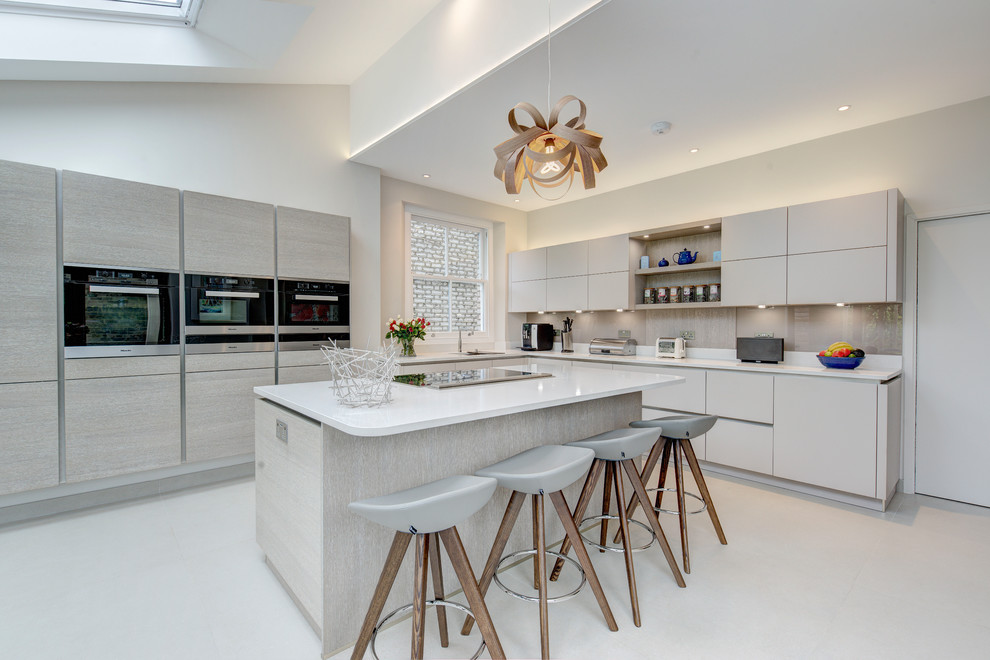 Photo of a large contemporary l-shaped kitchen in London with an undermount sink, flat-panel cabinets, grey cabinets, grey splashback, glass sheet splashback, black appliances and with island.