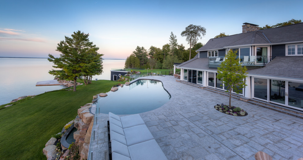 Traditional backyard custom-shaped infinity pool in Other with a hot tub and natural stone pavers.