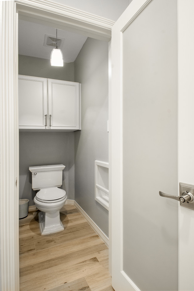 Design ideas for a mid-sized transitional powder room in Dallas with recessed-panel cabinets, white cabinets, a two-piece toilet, gray tile, marble, grey walls, porcelain floors, an undermount sink, engineered quartz benchtops, brown floor and white benchtops.