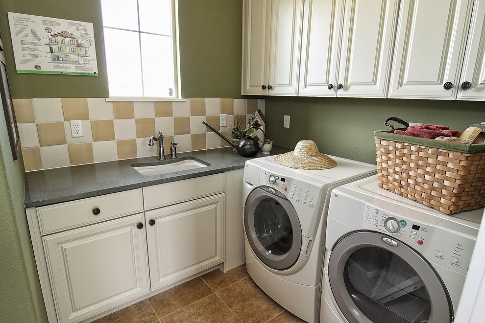 Photo of a mediterranean l-shaped dedicated laundry room in Denver with an undermount sink, raised-panel cabinets, white cabinets, solid surface benchtops, green walls, porcelain floors, a side-by-side washer and dryer and beige floor.