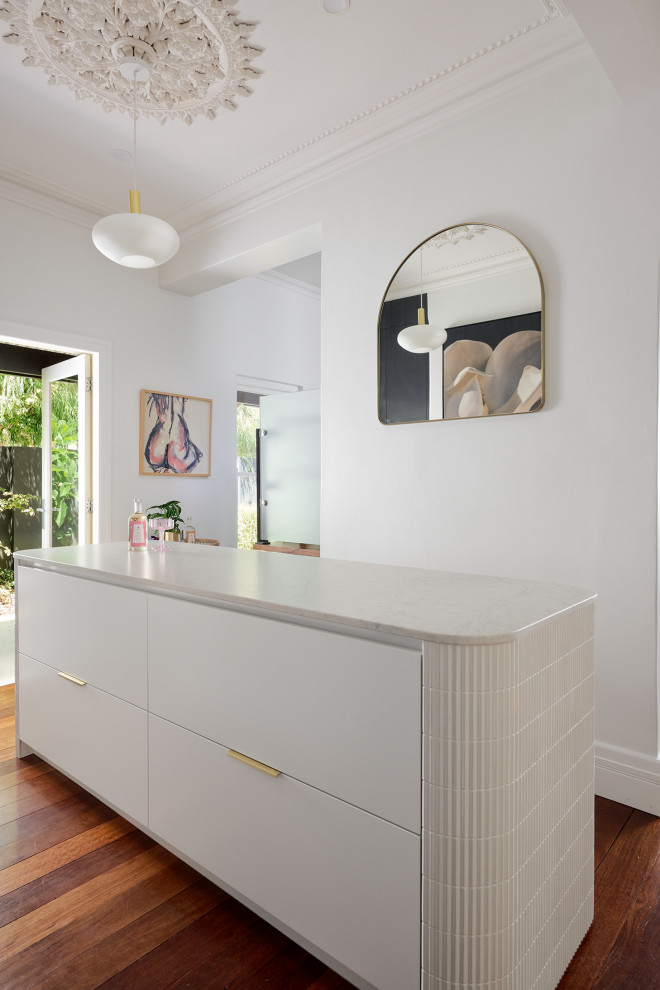 This is an example of a large modern galley kitchen in Perth with an undermount sink, flat-panel cabinets, white cabinets, quartz benchtops, white splashback, engineered quartz splashback, black appliances, dark hardwood floors, with island, brown floor and white benchtop.