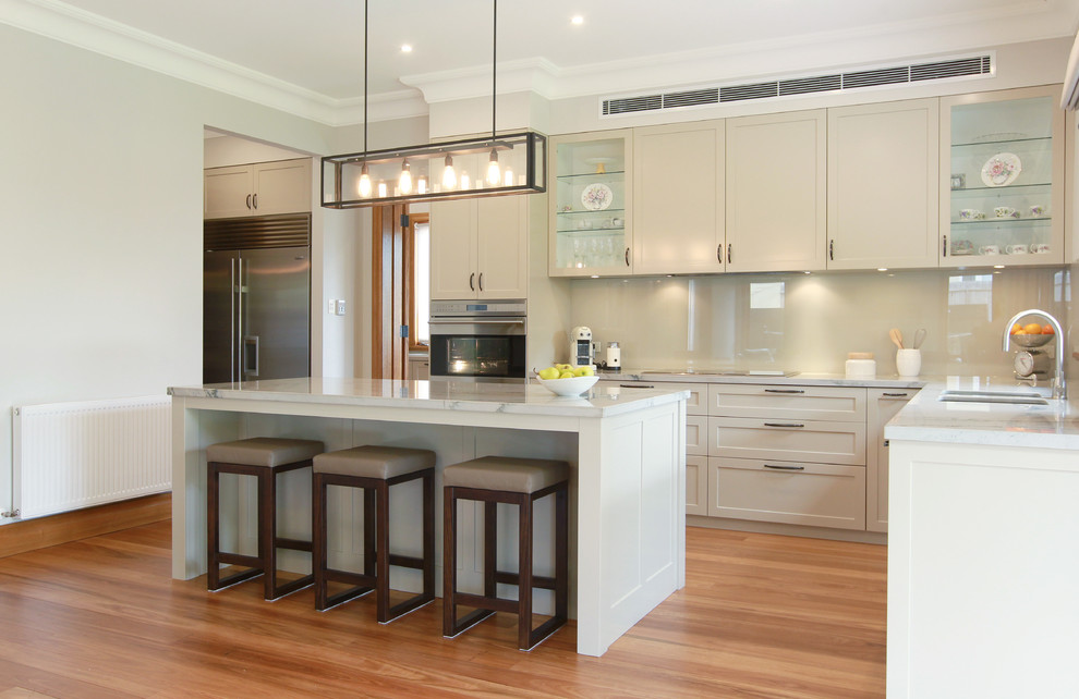 Design ideas for a large traditional galley eat-in kitchen in Melbourne with an undermount sink, shaker cabinets, beige cabinets, marble benchtops, beige splashback, glass sheet splashback, stainless steel appliances, medium hardwood floors and with island.