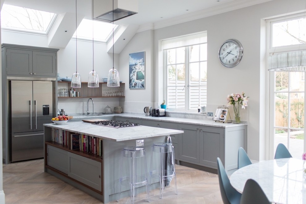 Design ideas for a transitional l-shaped eat-in kitchen in London with shaker cabinets, grey cabinets, white splashback, stainless steel appliances, light hardwood floors and with island.