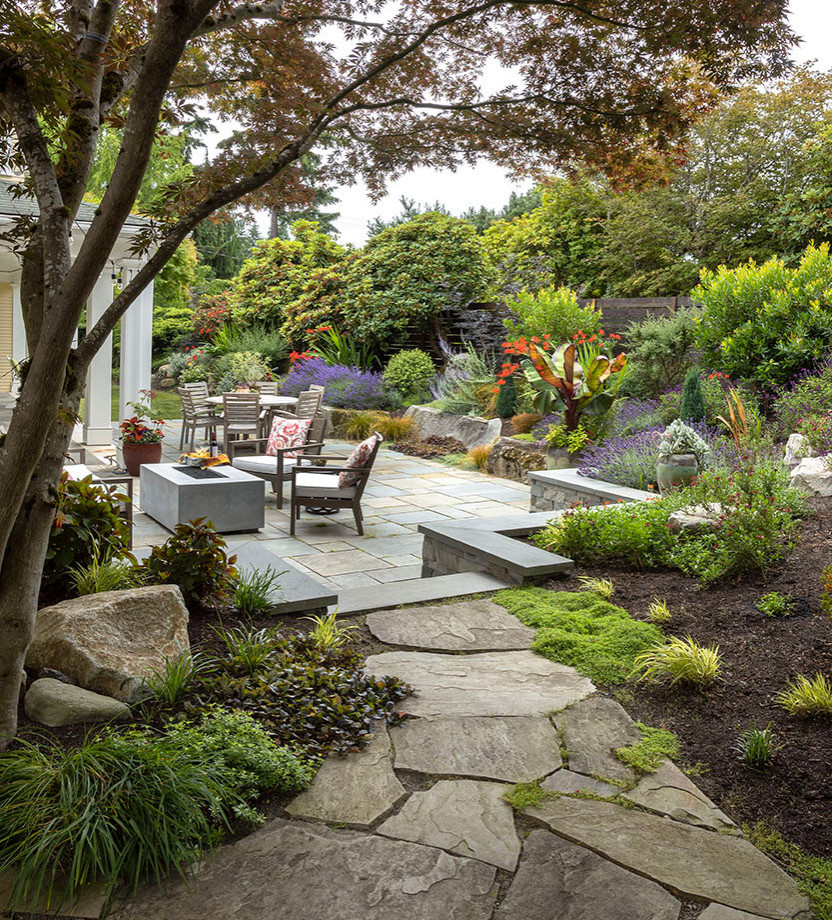 This is an example of a mid-sized country backyard full sun xeriscape in Seattle with natural stone pavers and a wood fence.