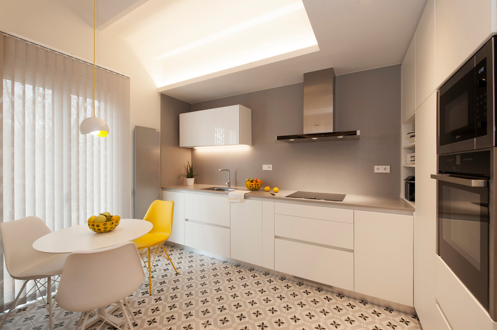 Inspiration for a mid-sized modern l-shaped eat-in kitchen in Barcelona with a single-bowl sink, flat-panel cabinets, white cabinets, quartz benchtops, grey splashback, black appliances, ceramic floors, no island and multi-coloured floor.