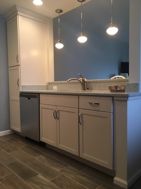 Photo of a mid-sized transitional galley kitchen in Raleigh with stainless steel appliances, an undermount sink, shaker cabinets, white cabinets, granite benchtops, vinyl floors, brown floor and grey benchtop.