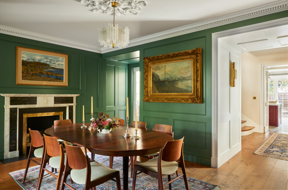 Photo of a large classic open plan dining room in London with green walls, medium hardwood flooring, a standard fireplace, a stone fireplace surround, brown floors, exposed beams and panelled walls.