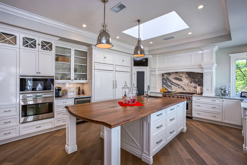 This is an example of a traditional u-shaped kitchen in Orange County with a farmhouse sink, shaker cabinets, white cabinets, stainless steel appliances, dark hardwood floors and with island.