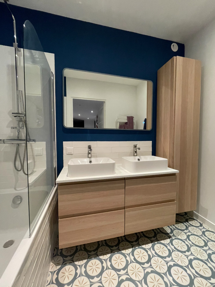 Photo of a mid-sized contemporary kids bathroom in Lyon with laminate benchtops, a double vanity, a floating vanity, beaded inset cabinets, light wood cabinets, an undermount tub, a shower/bathtub combo, a two-piece toilet, white tile, terra-cotta tile, blue walls, ceramic floors, a vessel sink, blue floor and white benchtops.