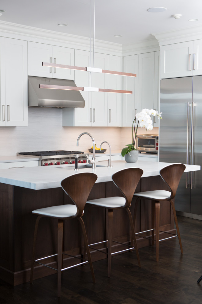 Design ideas for a transitional l-shaped kitchen in New York with shaker cabinets, white cabinets, white splashback, stainless steel appliances, dark hardwood floors, with island and marble benchtops.
