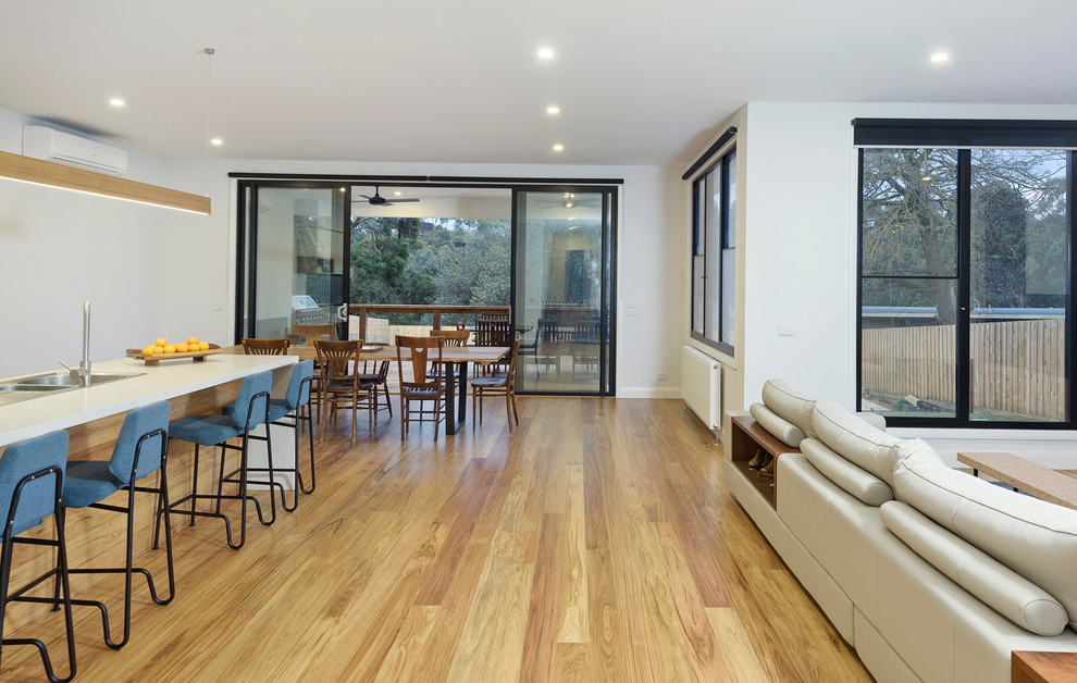 This is an example of a mid-sized contemporary galley eat-in kitchen in Melbourne with a double-bowl sink, flat-panel cabinets, white cabinets, quartz benchtops, glass sheet splashback, stainless steel appliances, light hardwood floors and with island.