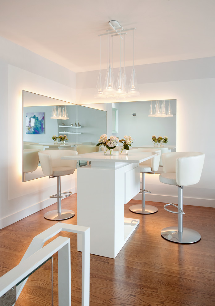 Photo of a mid-sized contemporary seated home bar in Boston with white cabinets, quartz benchtops, white splashback, medium hardwood floors, brown floor and white benchtop.