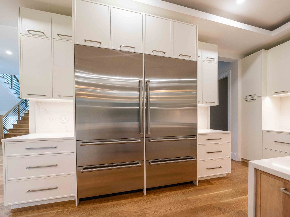 Kitchen - transitional light wood floor and tray ceiling kitchen idea in Boston with an undermount sink, shaker cabinets, quartz countertops, quartz backsplash, stainless steel appliances and two islands