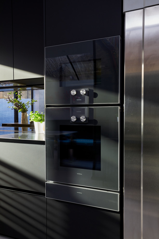 Small modern single-wall eat-in kitchen in London with flat-panel cabinets, black cabinets, stainless steel benchtops and with island.