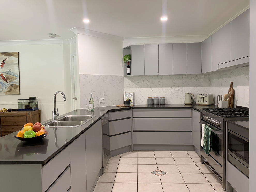 Inspiration for a mid-sized contemporary u-shaped open plan kitchen in Brisbane with a drop-in sink, flat-panel cabinets, grey cabinets, quartz benchtops, grey splashback, porcelain splashback, stainless steel appliances, terra-cotta floors, no island, beige floor and black benchtop.