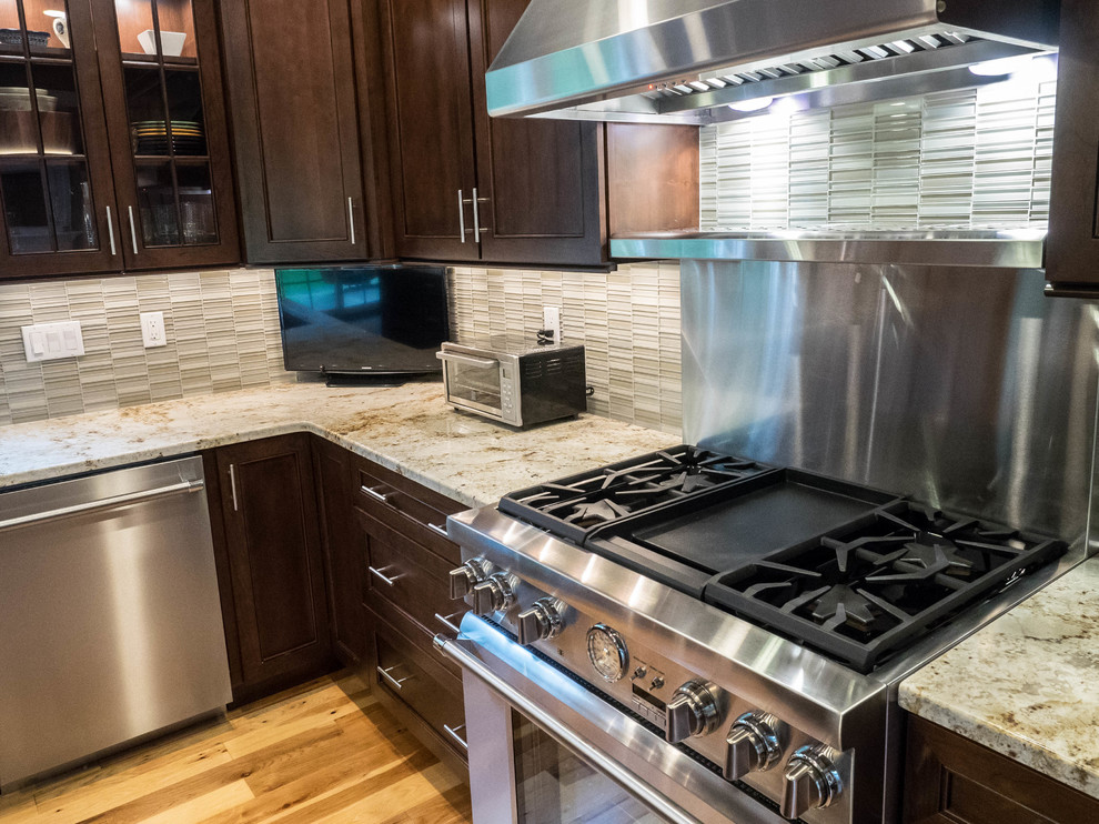 Example of a transitional medium tone wood floor kitchen design in New York with shaker cabinets, dark wood cabinets, granite countertops, green backsplash, glass tile backsplash and stainless steel appliances