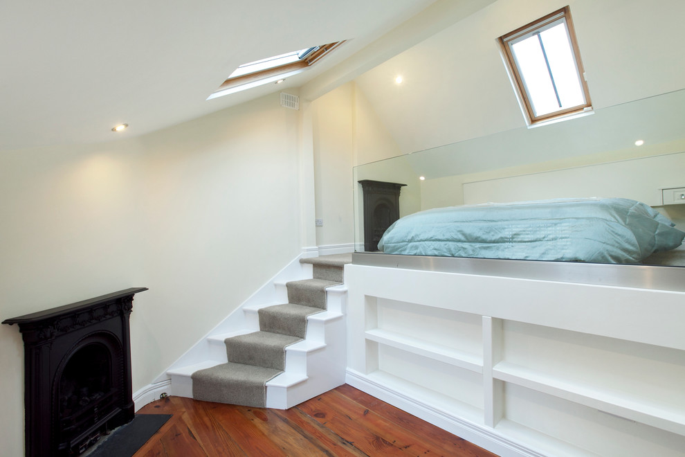 This is an example of a mid-sized modern loft-style bedroom in Dublin with white walls, medium hardwood floors, a standard fireplace and a metal fireplace surround.