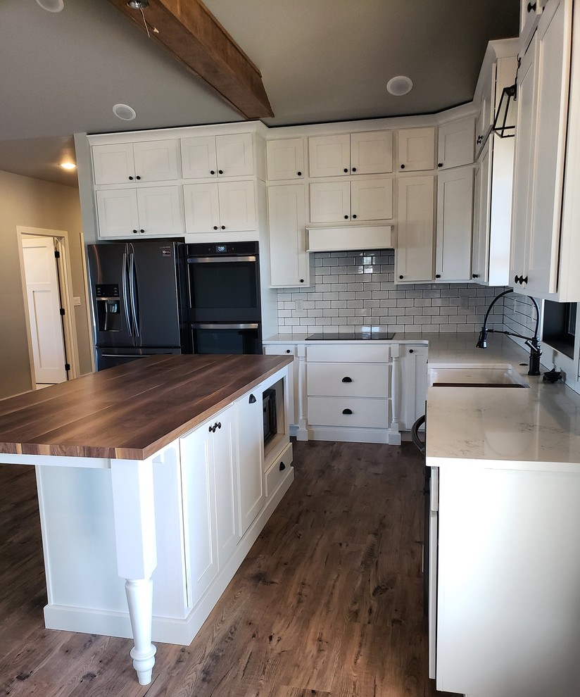 Design ideas for a mid-sized country l-shaped eat-in kitchen in Kansas City with a farmhouse sink, flat-panel cabinets, white cabinets, quartz benchtops, white splashback, subway tile splashback, stainless steel appliances, vinyl floors, with island, grey floor and white benchtop.