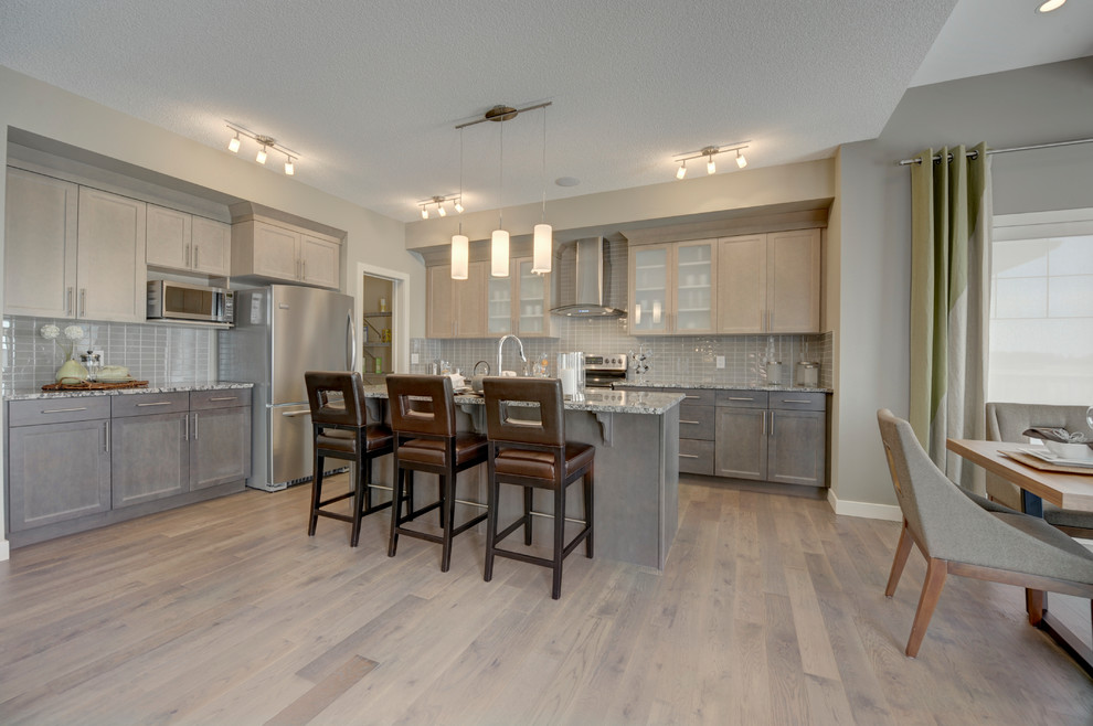 Mid-sized transitional l-shaped medium tone wood floor and brown floor eat-in kitchen photo in Edmonton with a double-bowl sink, shaker cabinets, brown cabinets, granite countertops, gray backsplash, ceramic backsplash, stainless steel appliances and an island