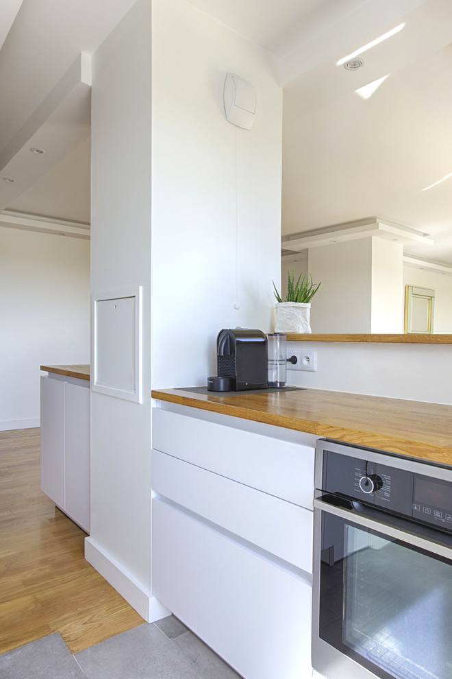 Small contemporary galley open plan kitchen in Paris with an undermount sink, white cabinets, wood benchtops, brown splashback, timber splashback, ceramic floors, grey floor and brown benchtop.