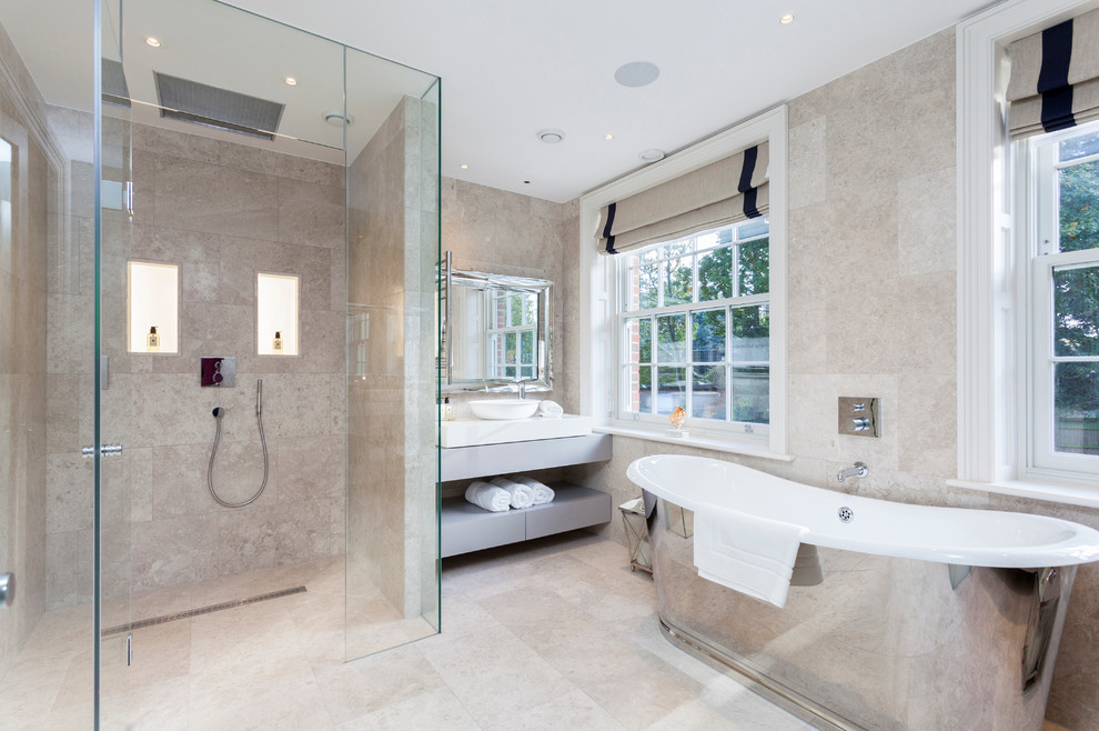 This is an example of a transitional bathroom in London with a vessel sink, open cabinets, grey cabinets, a freestanding tub, a corner shower and beige tile.