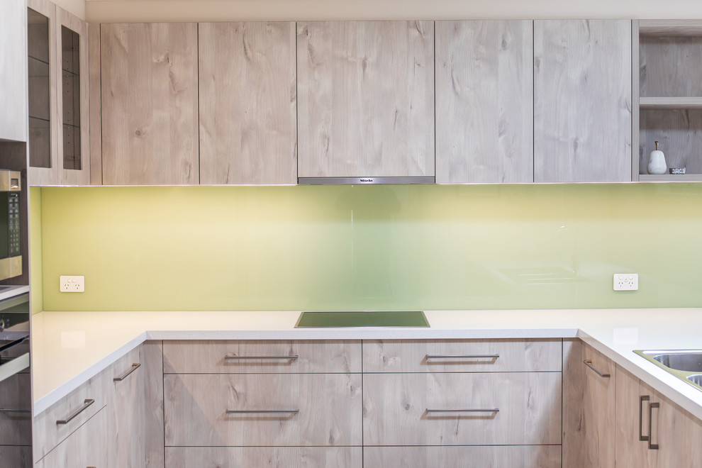 Design ideas for a mid-sized modern u-shaped kitchen pantry in Adelaide with a double-bowl sink, flat-panel cabinets, light wood cabinets, quartz benchtops, green splashback, glass sheet splashback, stainless steel appliances, porcelain floors, a peninsula, white floor and white benchtop.