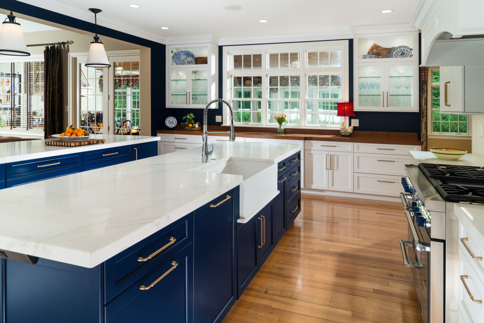 Example of a huge transitional u-shaped brown floor kitchen design with a farmhouse sink, shaker cabinets, quartz countertops, white backsplash, quartz backsplash, stainless steel appliances, two islands and white countertops