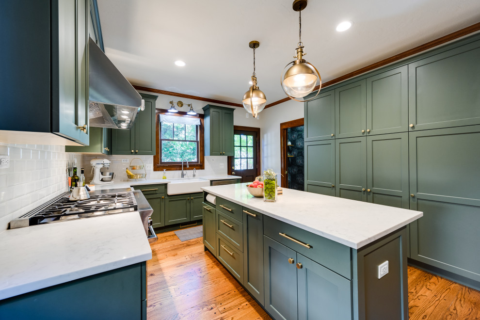 Mid-sized arts and crafts l-shaped kitchen in Oklahoma City with a farmhouse sink, shaker cabinets, green cabinets, quartz benchtops, yellow splashback, ceramic splashback, stainless steel appliances, medium hardwood floors, with island, brown floor and white benchtop.
