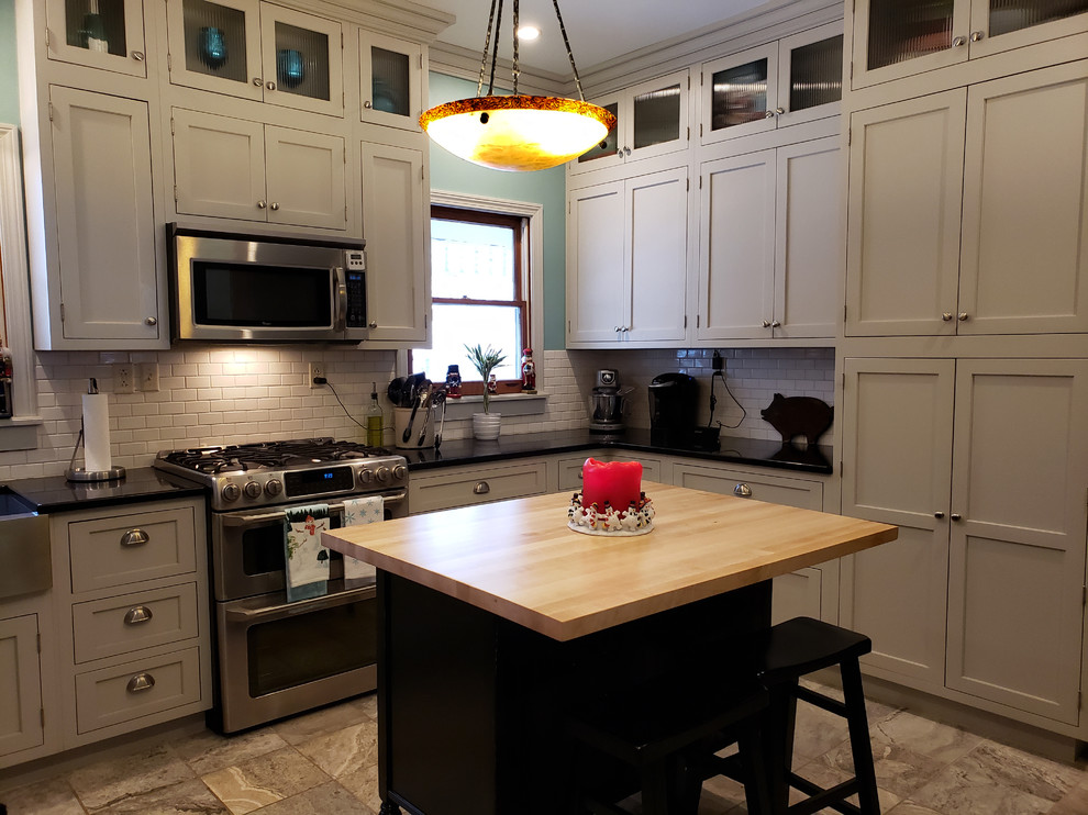 Inspiration for a large transitional u-shaped ceramic tile and beige floor kitchen pantry remodel with a farmhouse sink, recessed-panel cabinets, gray cabinets, quartz countertops, white backsplash, subway tile backsplash, stainless steel appliances, an island and black countertops