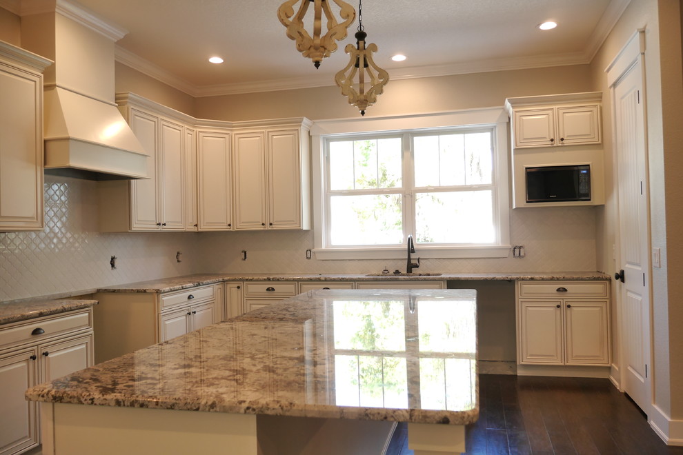 Inspiration for a traditional l-shaped open plan kitchen in Tampa with a single-bowl sink, raised-panel cabinets, white cabinets, granite benchtops, white splashback, ceramic splashback, stainless steel appliances, dark hardwood floors, with island and brown floor.