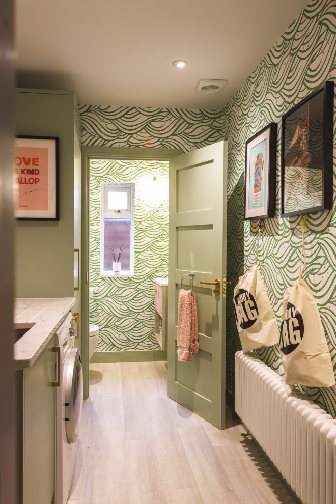 Example of a small trendy single-wall light wood floor, gray floor and wallpaper dedicated laundry room design in Berkshire with an integrated sink, flat-panel cabinets, green cabinets, quartzite countertops, pink backsplash, ceramic backsplash, green walls, a side-by-side washer/dryer and white countertops