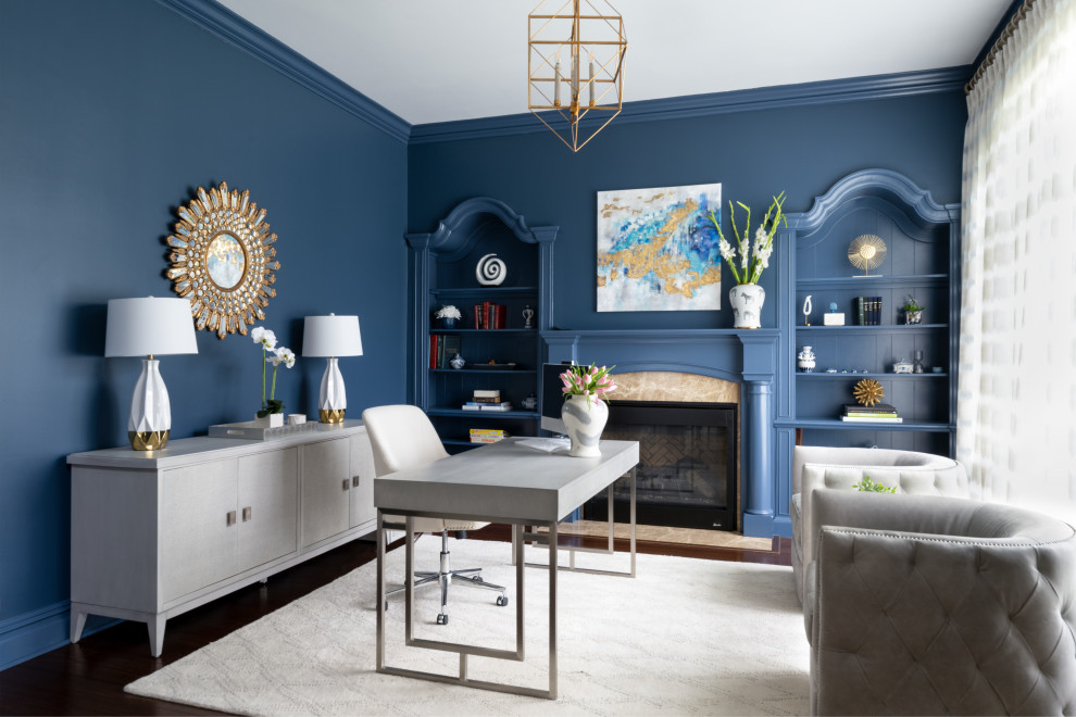 Klassisk inredning av ett mellanstort arbetsrum, med ett bibliotek, blå väggar, mörkt trägolv, en standard öppen spis, en spiselkrans i sten, ett fristående skrivbord och brunt golv
